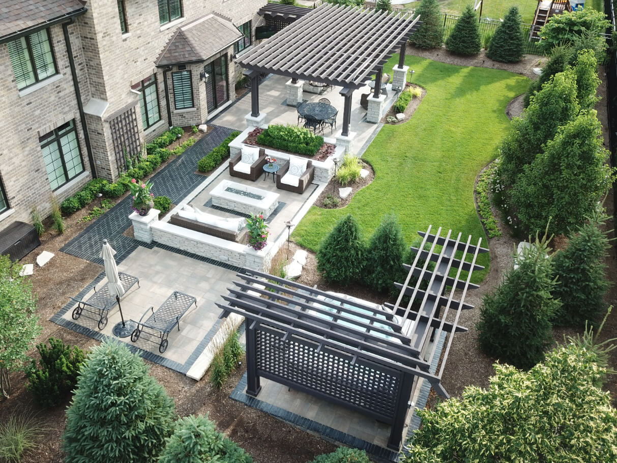 Completed backyard landscape project showing pergola, pavers, firepit, and plantings.