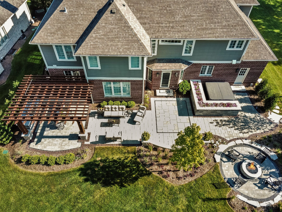Completed backyard landscape project showing pergola, pavers, firepit, and plantings.